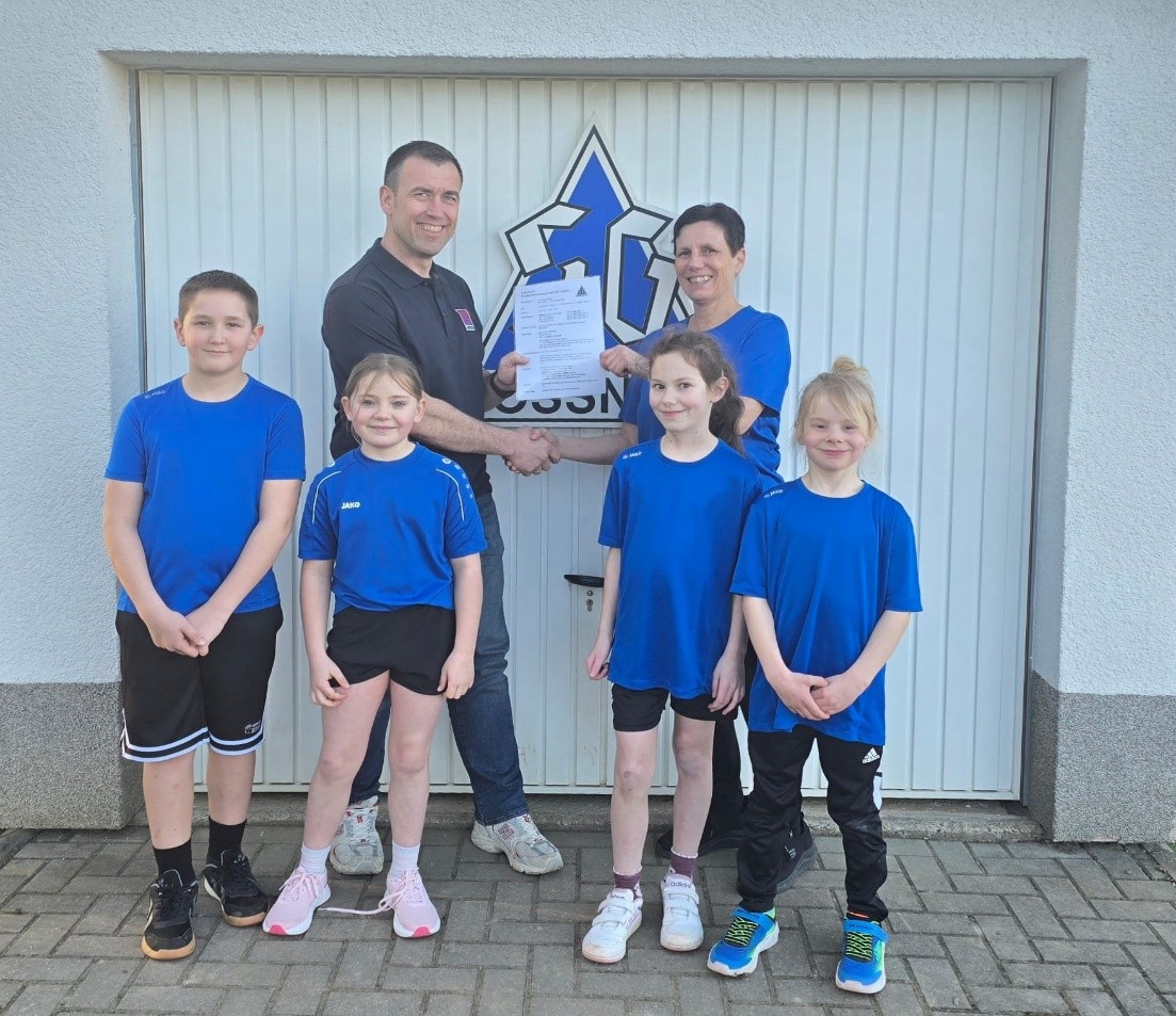 Übergabe der Ausschreibung für das Jahr 2026: Nicole Gruber (Trainerin der SG Jößnitz) übergibt die Ausschreibung an Andreas Rudolph (Leitung Anwendungstechnik Tageslichtsysteme LAMILUX). Mit auf dem Bild sind Kinder der Abteilung Leichtathletik.